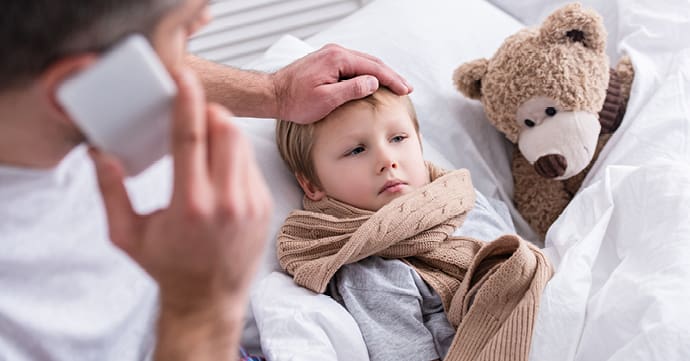 A parent with one hand on their toddlers forhead calls a nurse's hotline