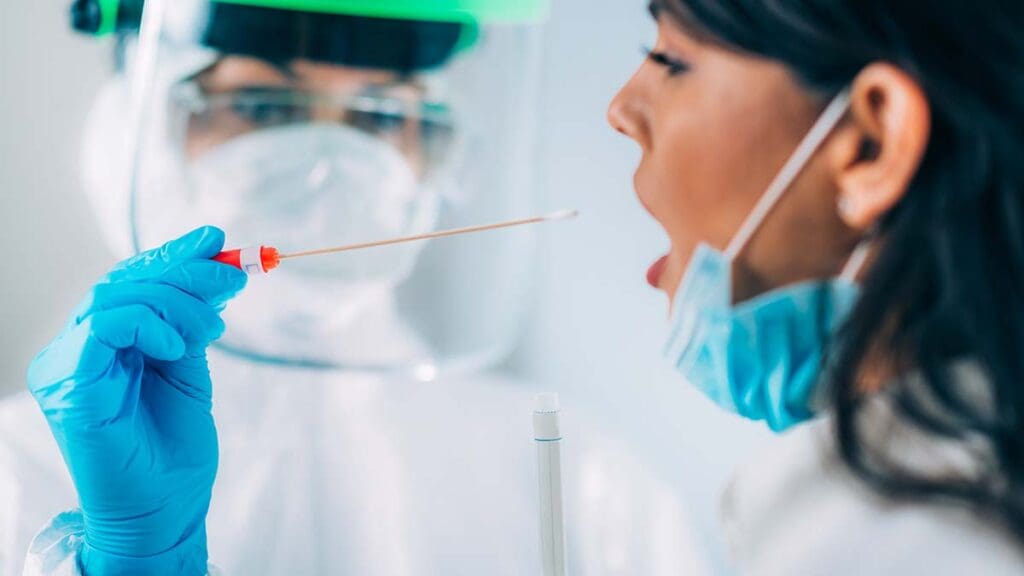 A healthcare worker in full PPE swabs the mouth of a patient