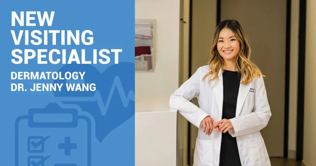 A woman in a white coat stands smiling next to a sign that reads, New Visiting Specialist Dermatology Dr. Jenny Wang.